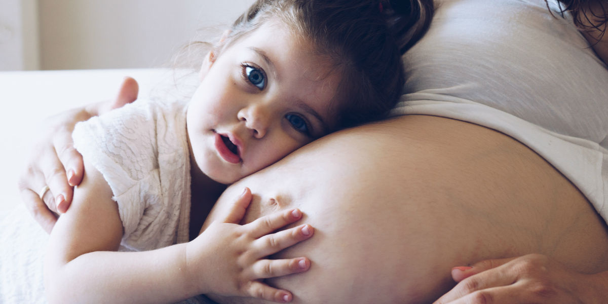 Una bimba ascolta il pancione della mamma