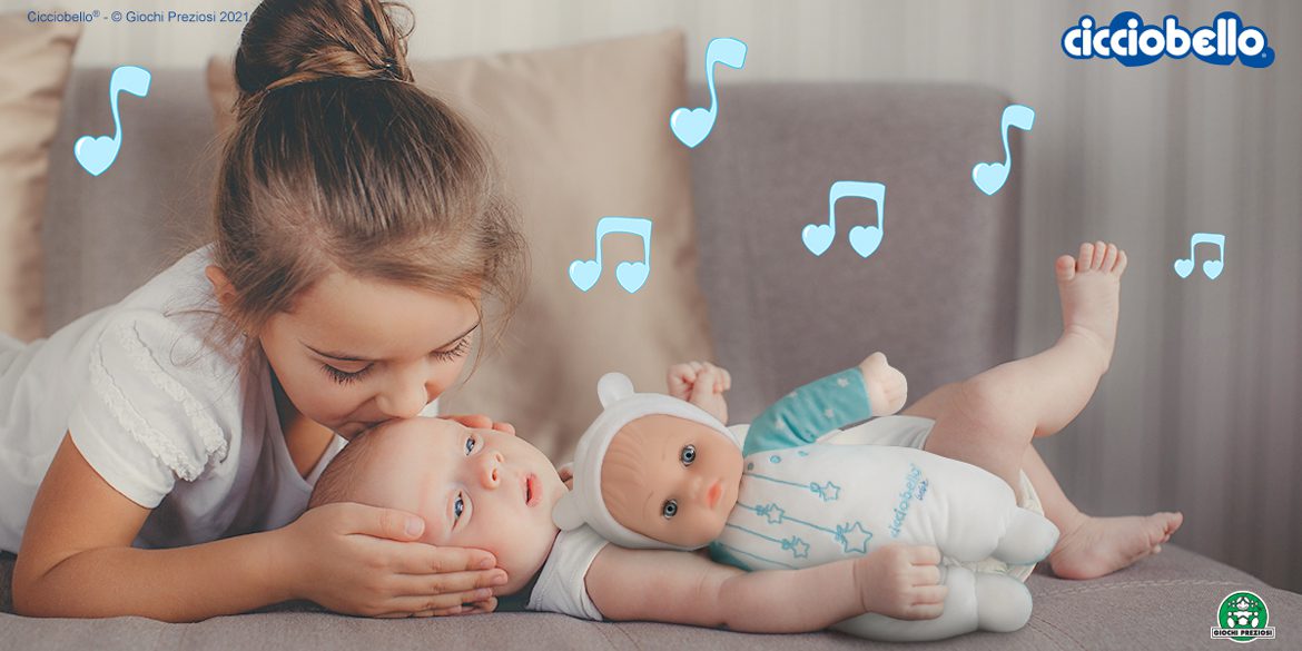 Sorella maggiore bacia sulla fronte il fratellino neonato, che stringe Cicciobello Bebè Carillon