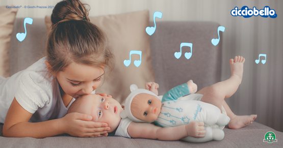 Sorella maggiore bacia sulla fronte il fratellino neonato, che stringe Cicciobello Bebè Carillon